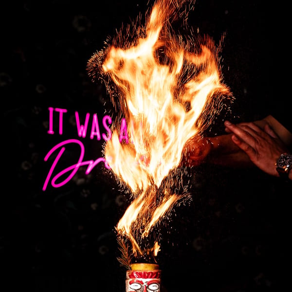 Flaming tiki cocktail with sparks against a dark background and pink neon sign.