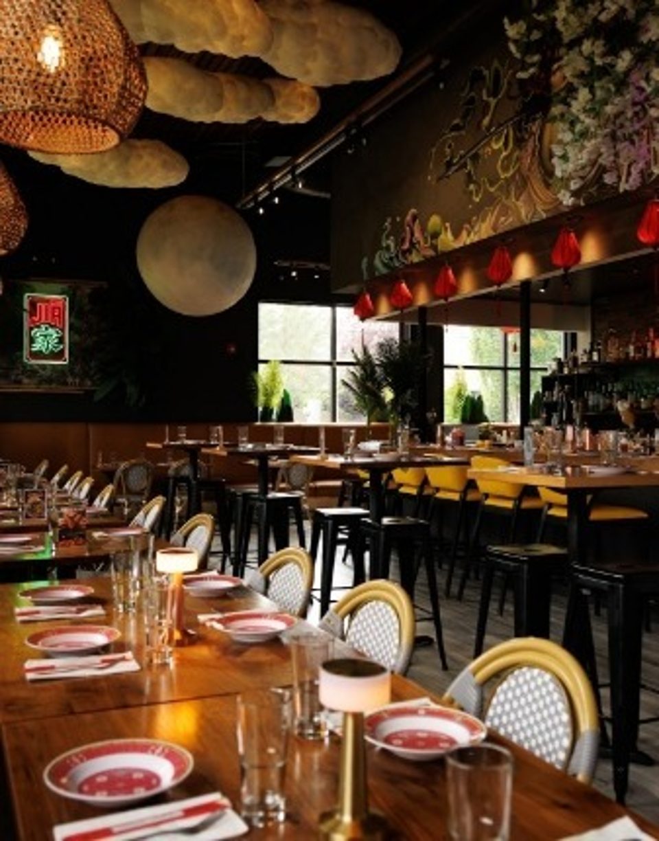 Modern restaurant interior with long wooden tables, cloud-like ceiling decor, and a large moon art piece.