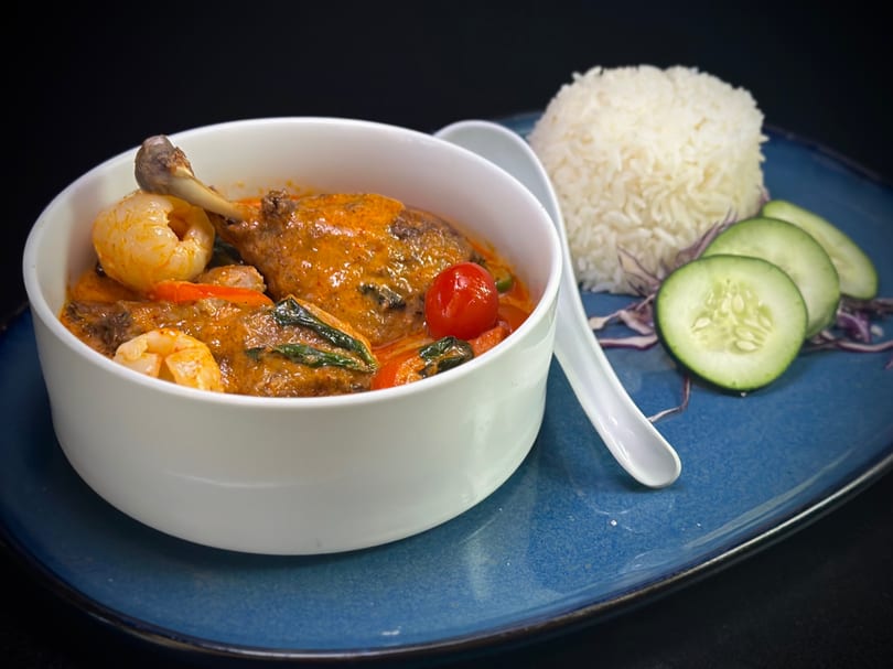 Red curry with duck leg, shrimp, cherry tomato, and basil, served with rice and cucumber.