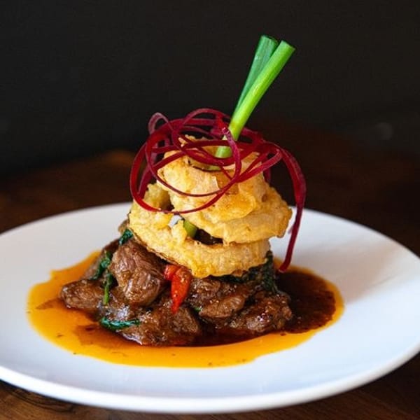 Braised meat dish with a rich sauce, topped with crispy onion rings, red garnish, and green onion.