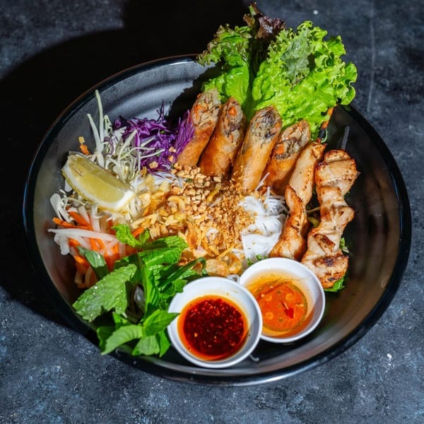 Vietnamese vermicelli bowl with spring rolls, grilled chicken, fresh vegetables, and dipping sauces.